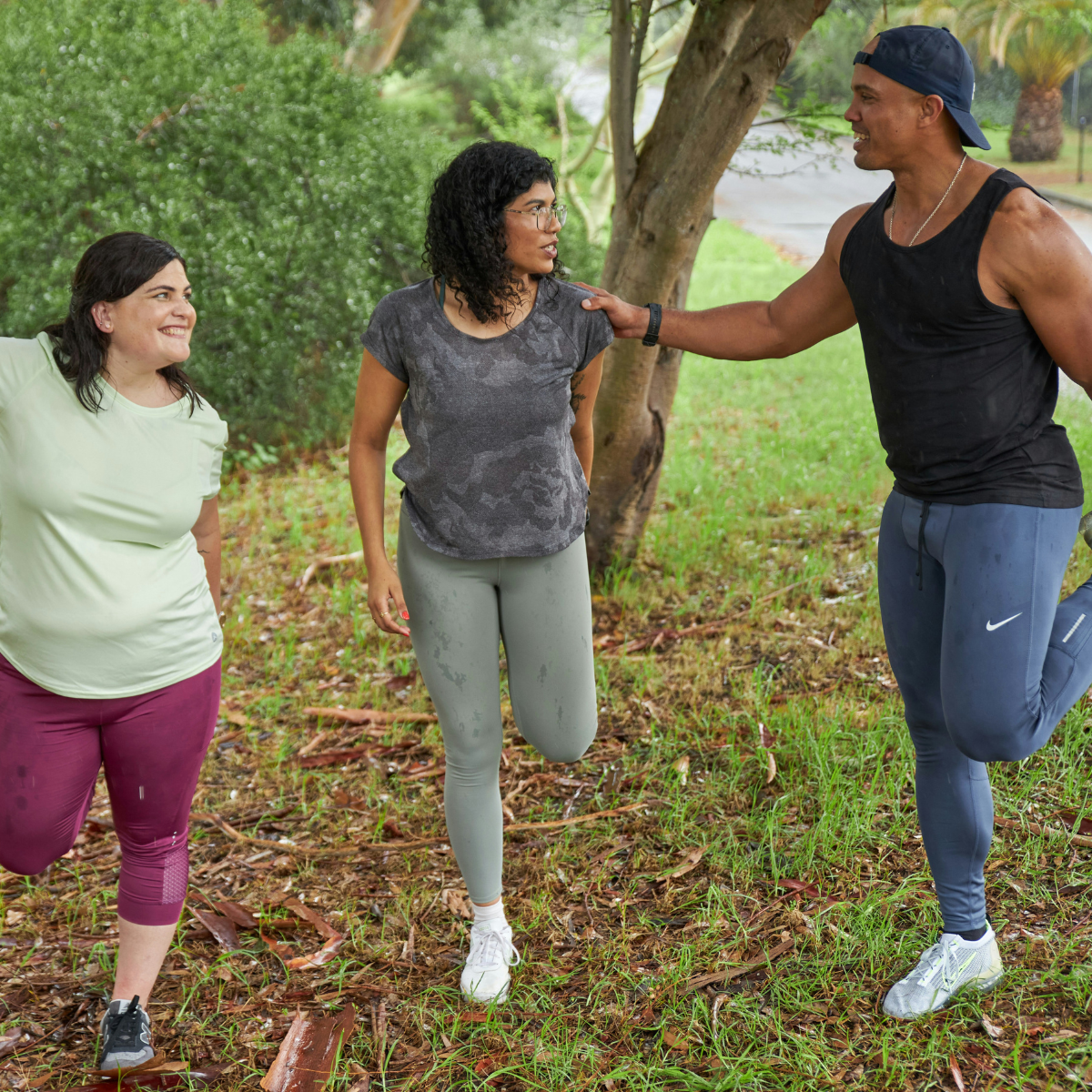 Three people in jogging clothes stand and stretch their calves before a run on a rainy day. 