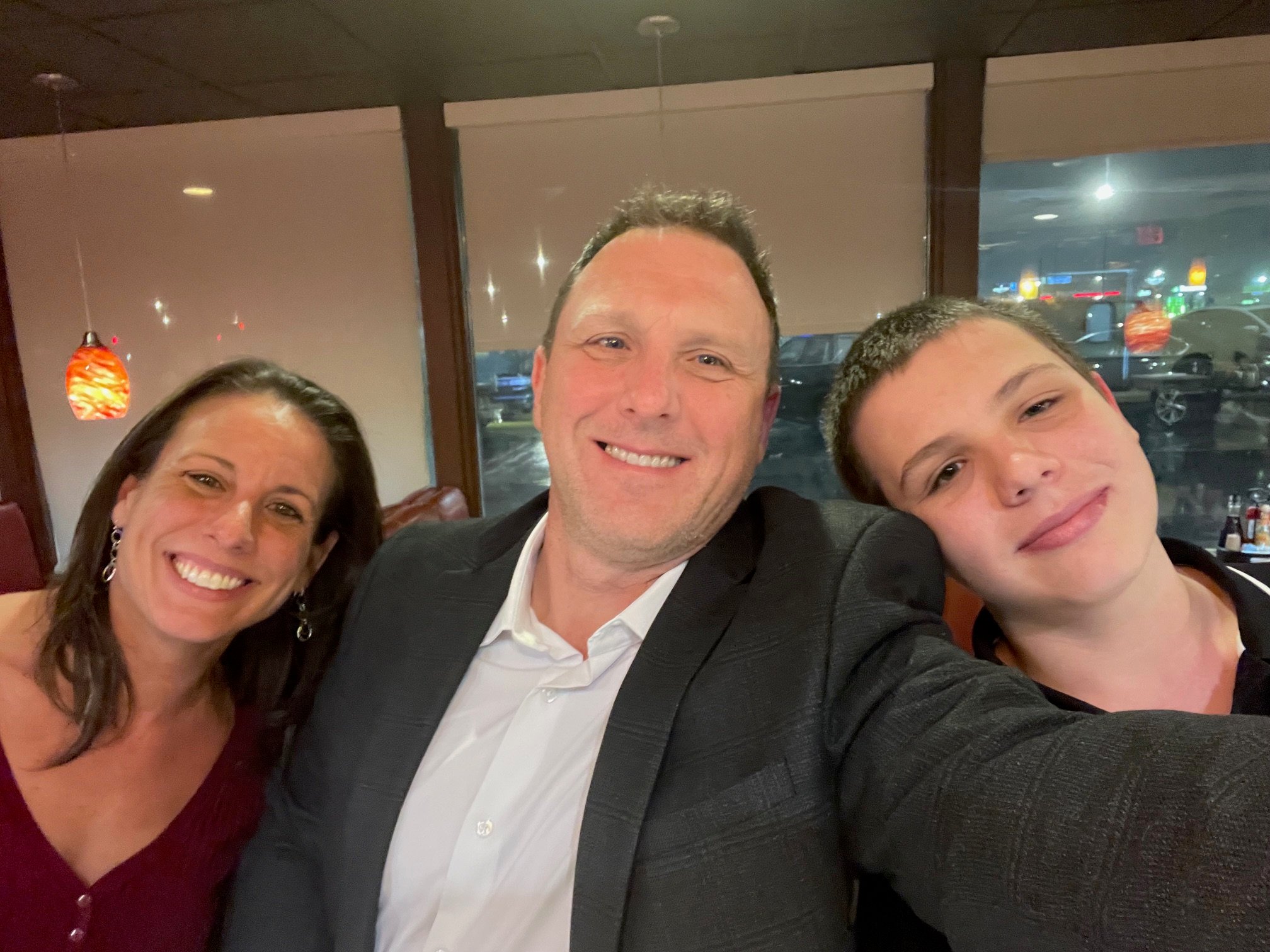 A man in dress shirt and suit jacket takes selfie with wife and son.