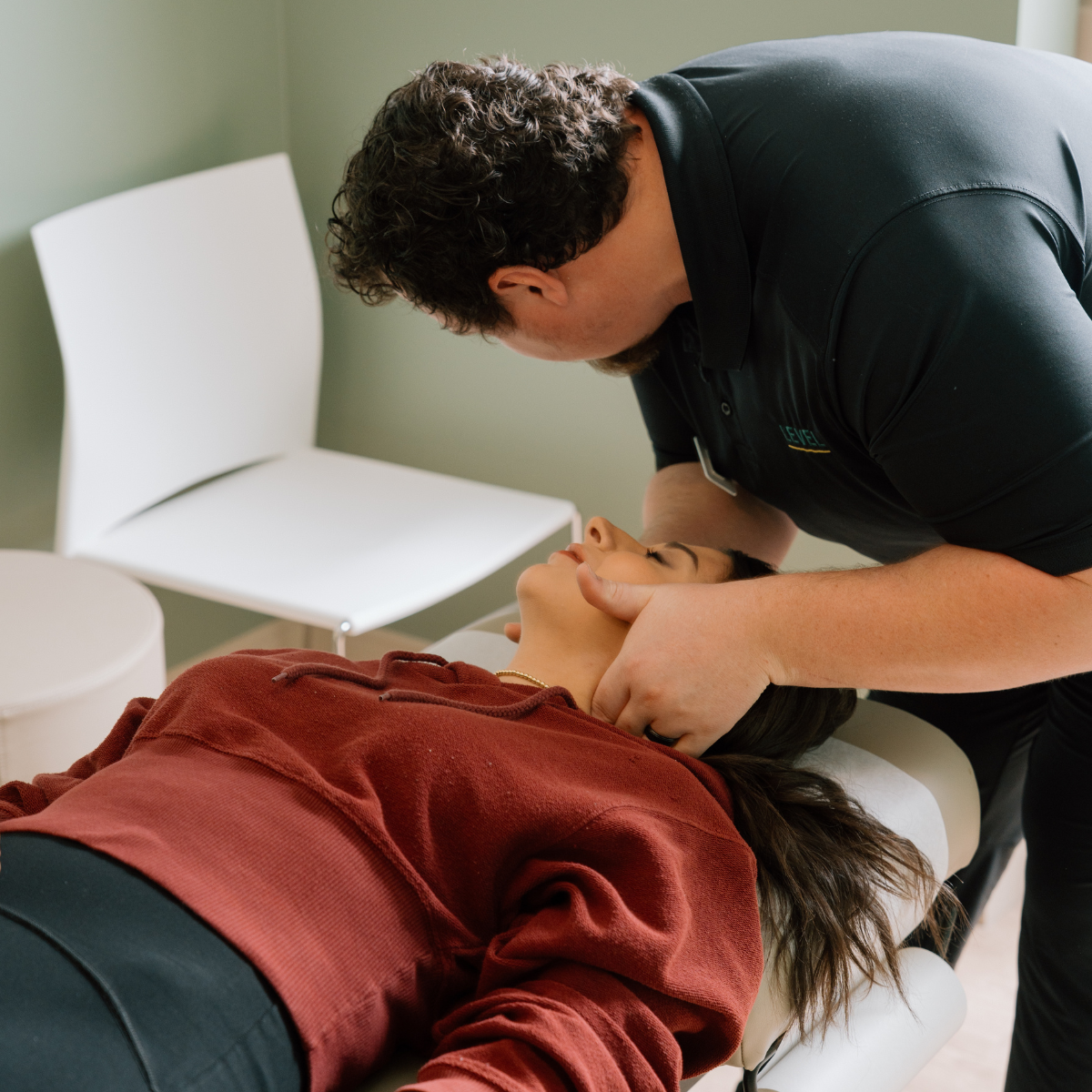 A chiropractor gently adjusts a woman's neck as she lies on a treatment table in a serene room with soft lighting and minimal decor.