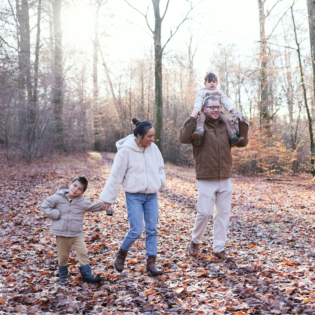 Family of four walking on a woodsy path covered with autumn leaves.