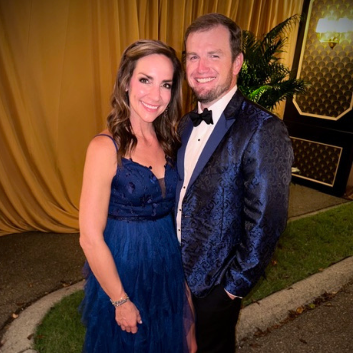 A woman in a formal blue dress and man in blue tuxedo jacket smile for the camera.