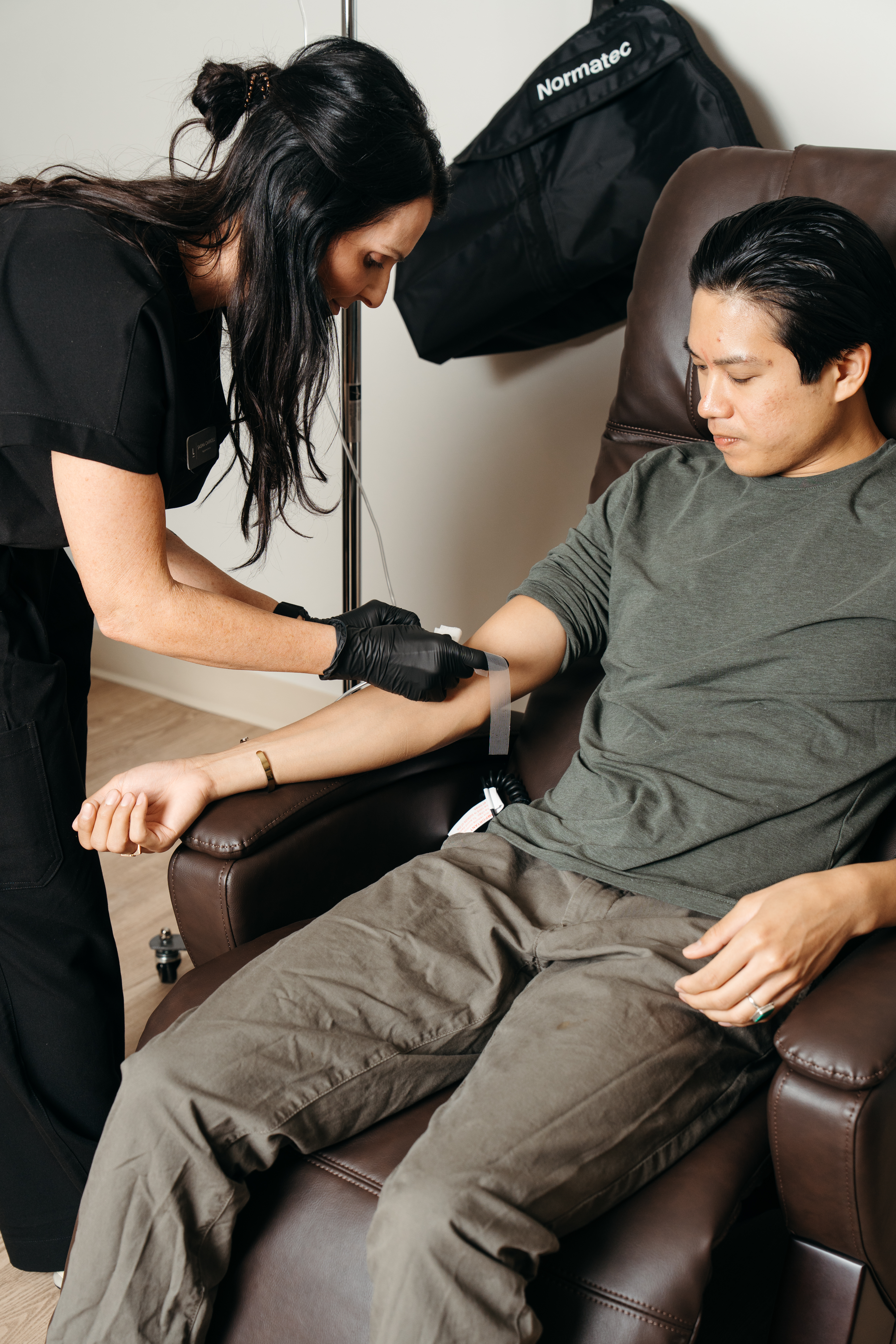 A Level Wellness practitioner prepares to draw blood from a seated man in a studio clinic decorated in earth tones.