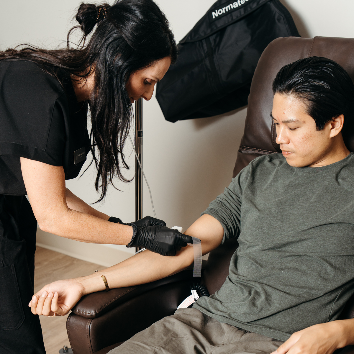 A Level Wellness practitioner prepares to draw blood from a seated man in a studio clinic decorated in earth tones.