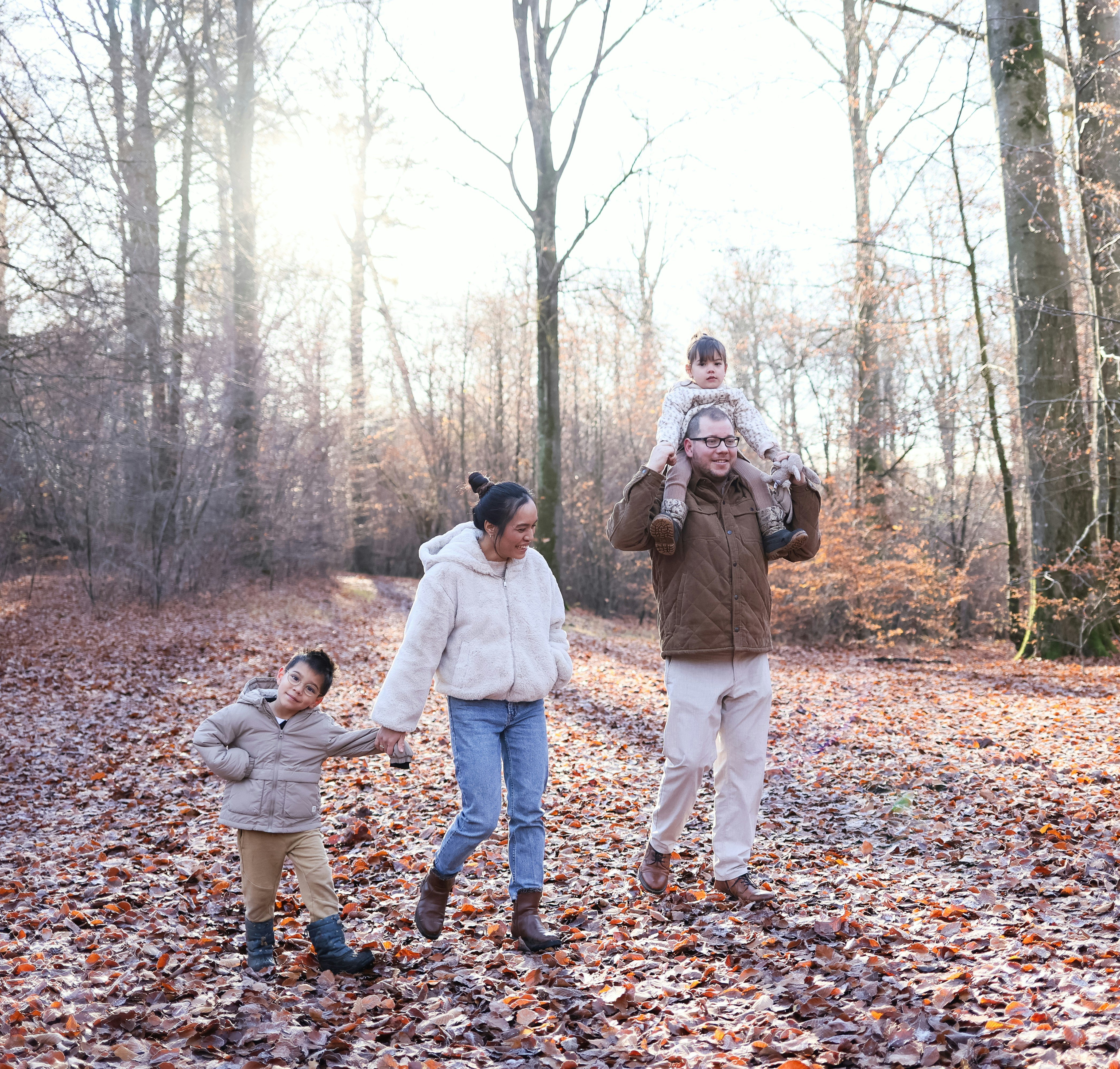 Family of four walking on a woodsy path covered with autumn leaves.