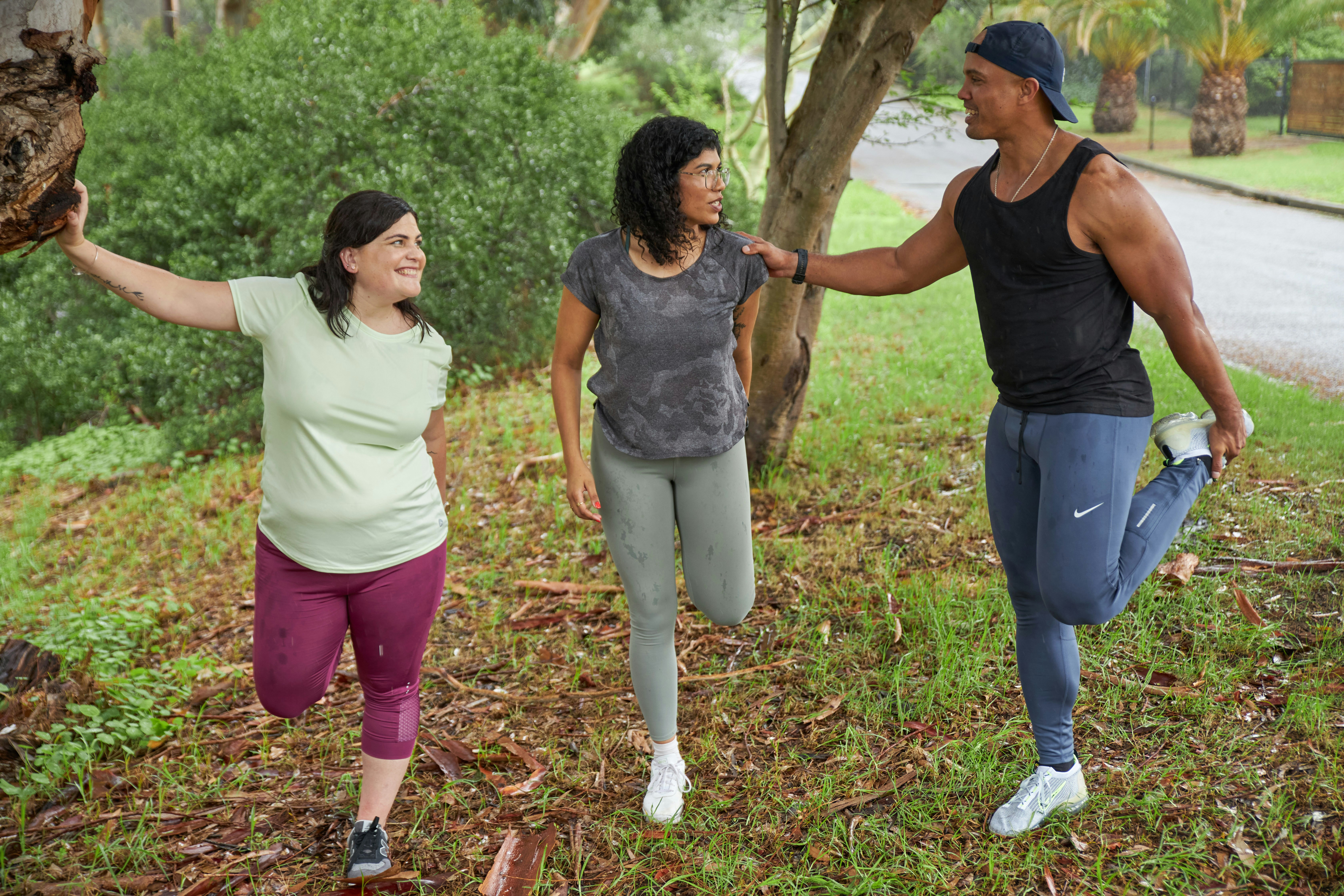 Three people in jogging clothes stand and stretch their calves before a run on a rainy day. 